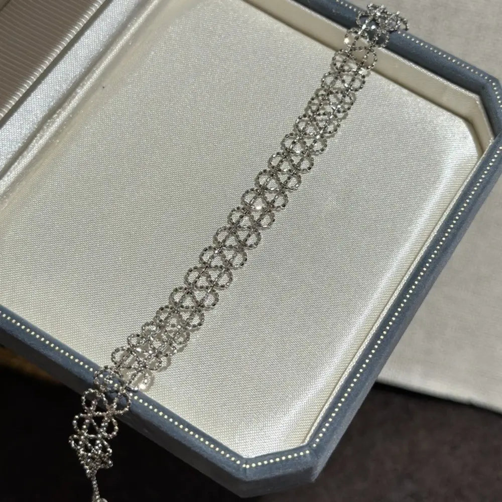A delicate silver-toned metal lace bracelet featuring an intricate repeating geometric pattern with embedded clear crystals designed as adjustable fashion jewelry.
