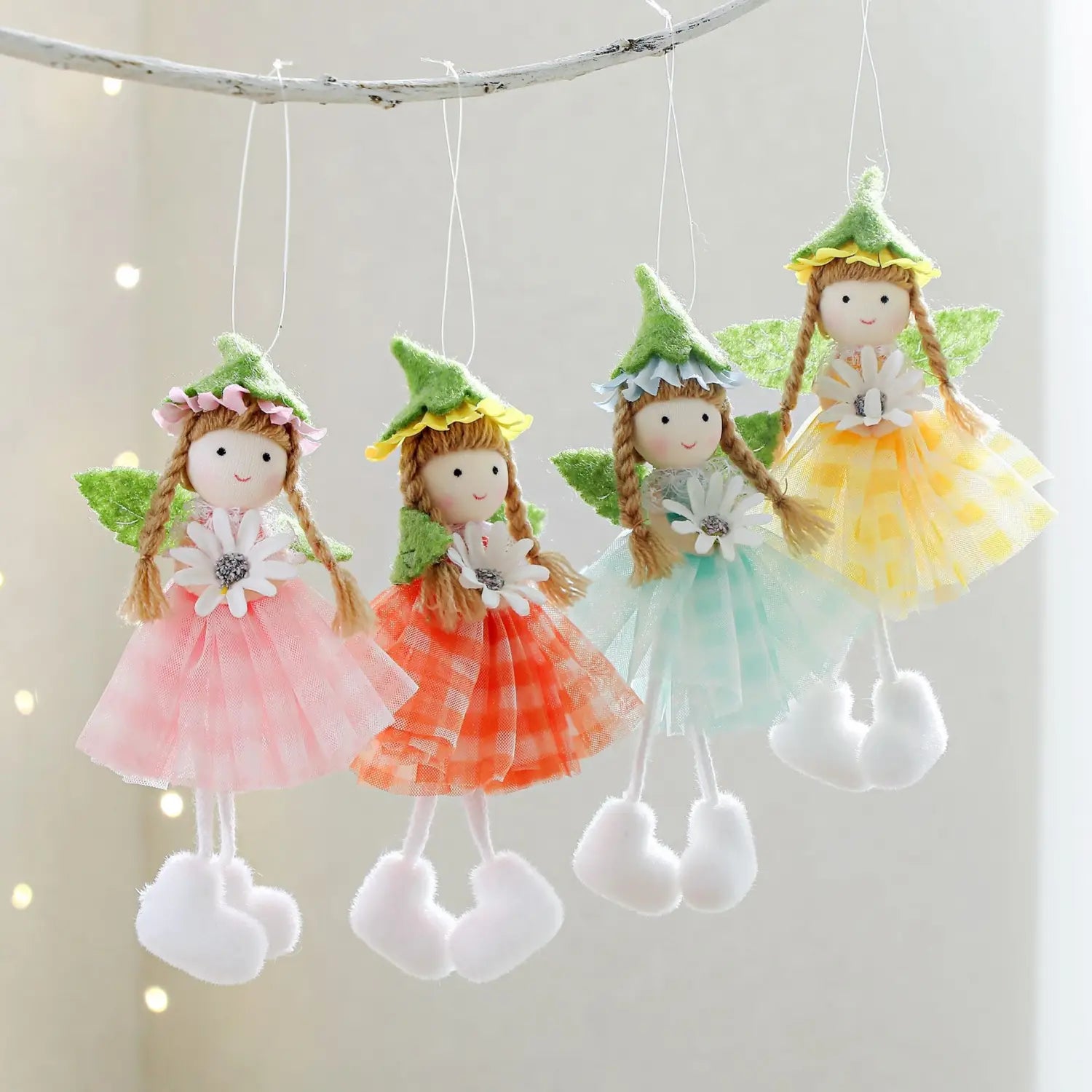 four handmade easter fairy hanging ornaments each with a green felt hat, wings, and colorful tulle skirts in pink, orange plaid, mint, and yellow polka dot holding white daisies