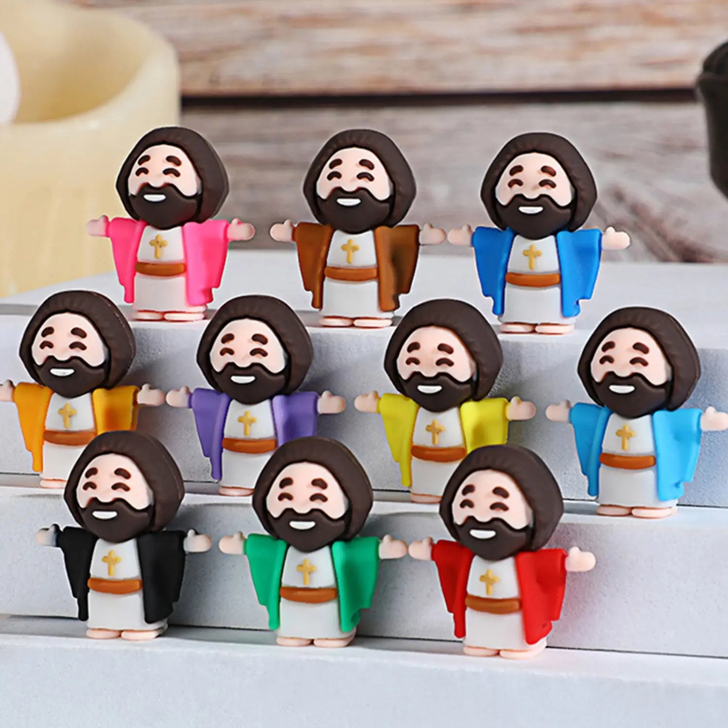 A collection of colorful cartoon-style mini jesus figurines with brown hair and beards wearing white robes with gold crosses and various colored outer garments ideal as easter party favors 10 pcs.
