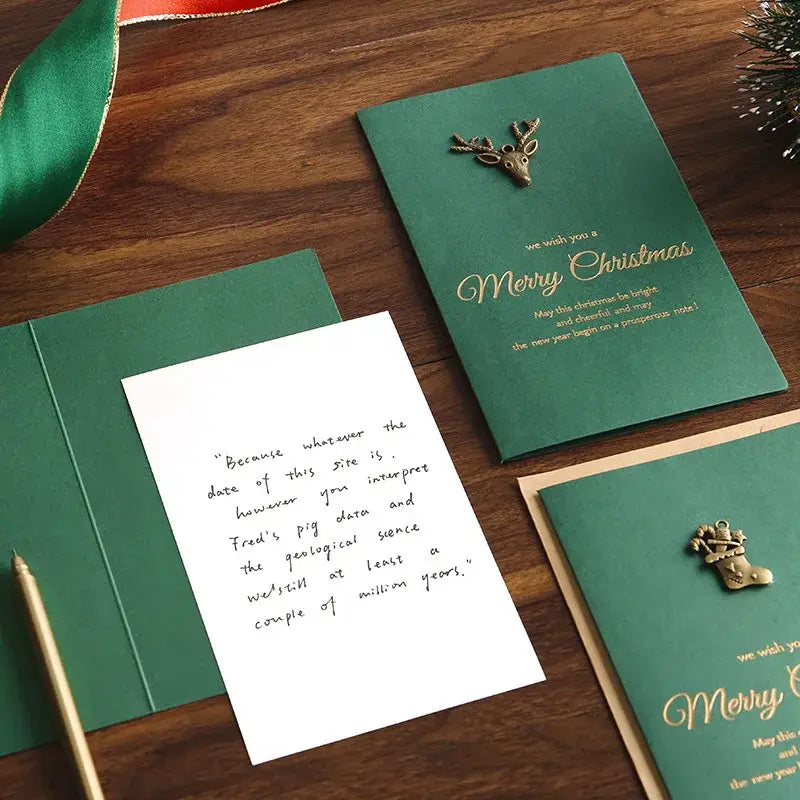 Emerald green christmas greeting card with gold foil lettering and a metallic deer pin included in a set with gold foil envelopes.