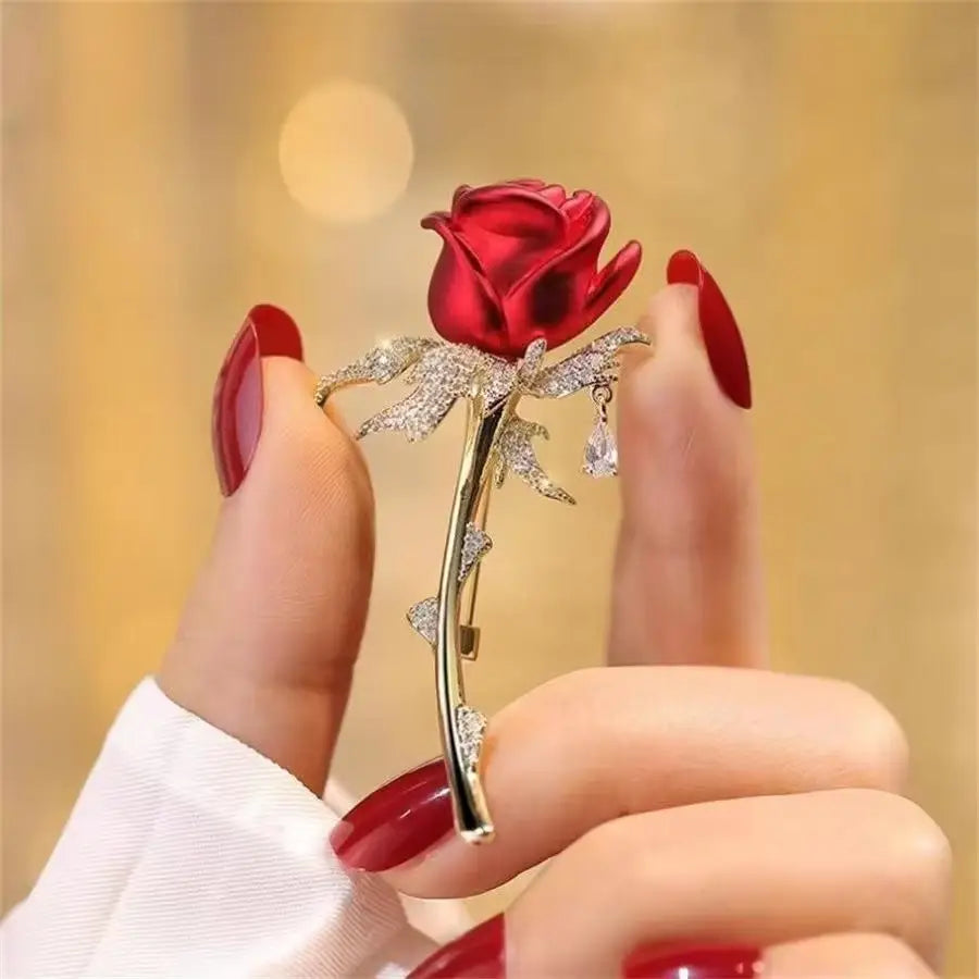 Broche en forme de rose en zircon rouge éclatant, avec des feuilles et une tige au ton argenté, ornée de cristaux transparents sur les pétales et d’un cristal en forme de goutte suspendue.
