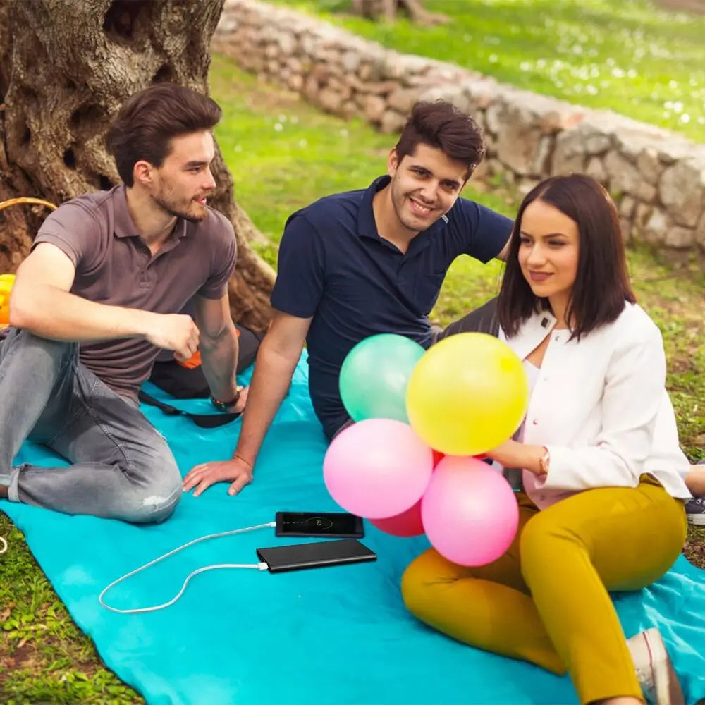 Globos de látex de colores agrupados sobre una manta de picnic azul, que complementan un banco de energía portátil de 20000 mAh diseñado para prendas térmicas.