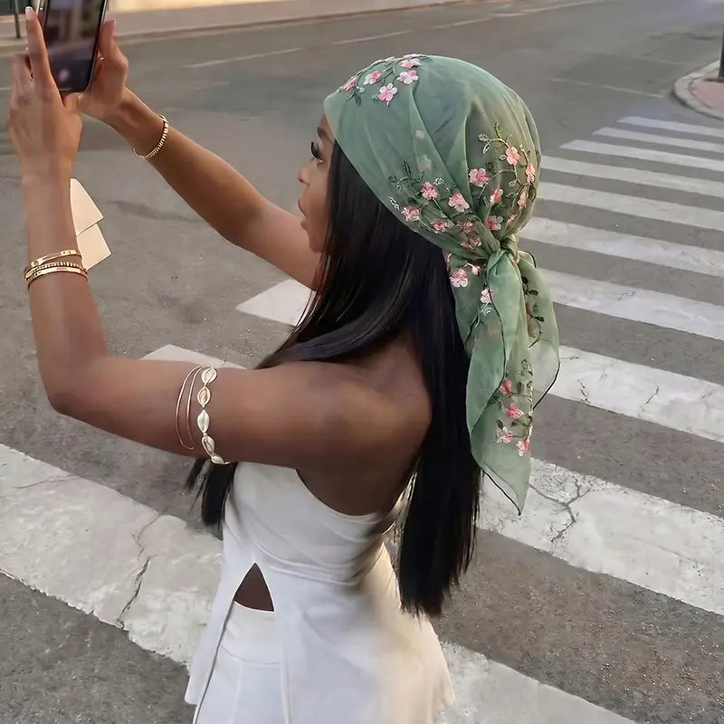 Un foulard châle hijab en dentelle florale en soie vert menthe délicat, avec des broderies florales roses, noué avec élégance autour de la tête.