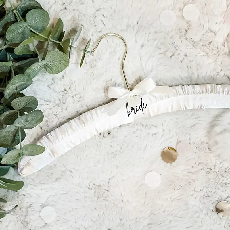 White satin bridal hanger with a delicate bow and bride scripted in black for wedding dress display.