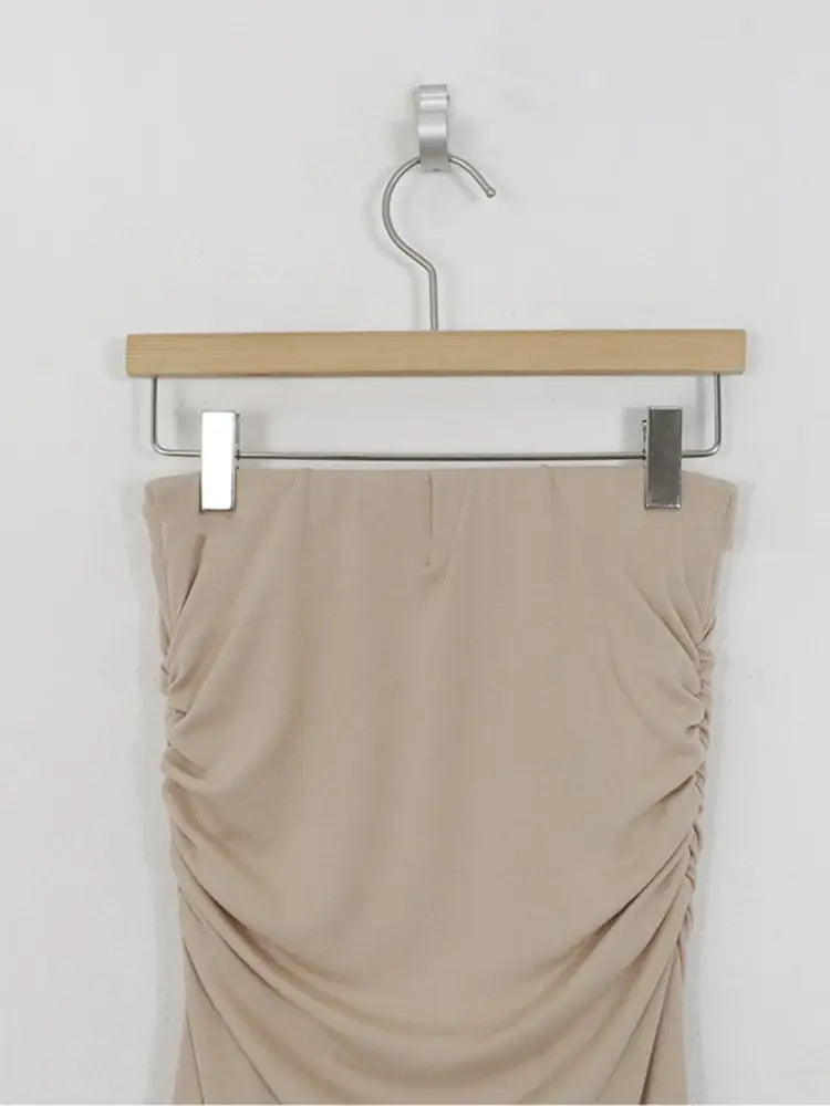 Beiger geraffter Meerjungfrauen-Midirock mit hoher Taille aus Stoff, der an einem Holzkleiderbügel mit Metallclips befestigt ist.