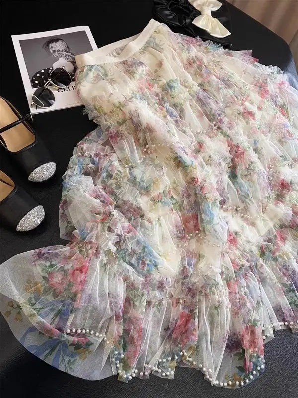Una falda de tul floral fairycore delicada en tonos pastel suaves, con tejido translúcido de múltiples capas y ribete de perlas a lo largo del bajo.