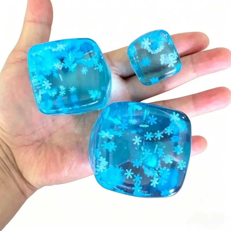 drei durchscheinende blaue quadratische Harz-Eiswürfel Stressabbau-Spielzeugwürfel mit eingebetteten Schneeflocken-Designs, von vorne betrachtet