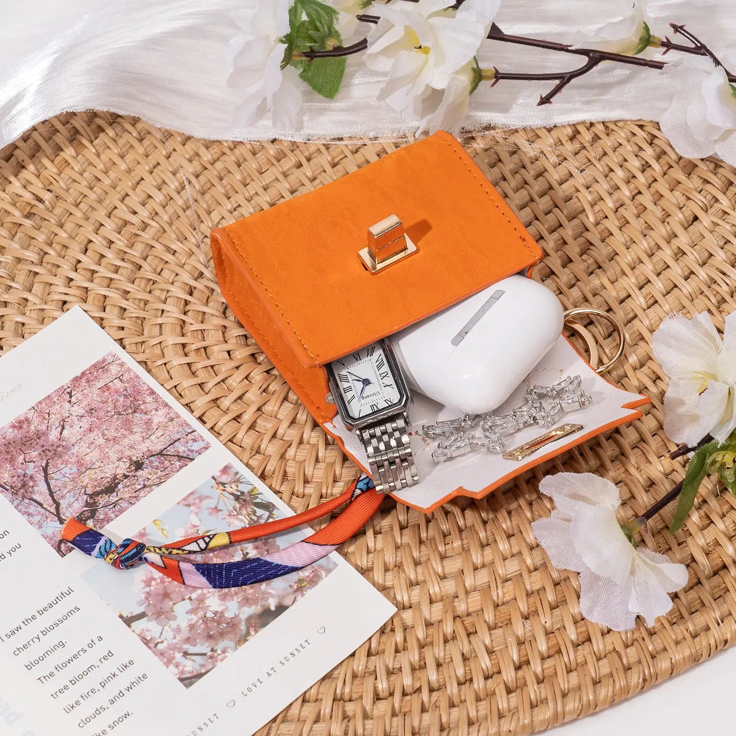 Miniature handbag keychain featuring an orange faux leather mini clutch with gold-tone clasp and white interior lining paired with a silk scarf.