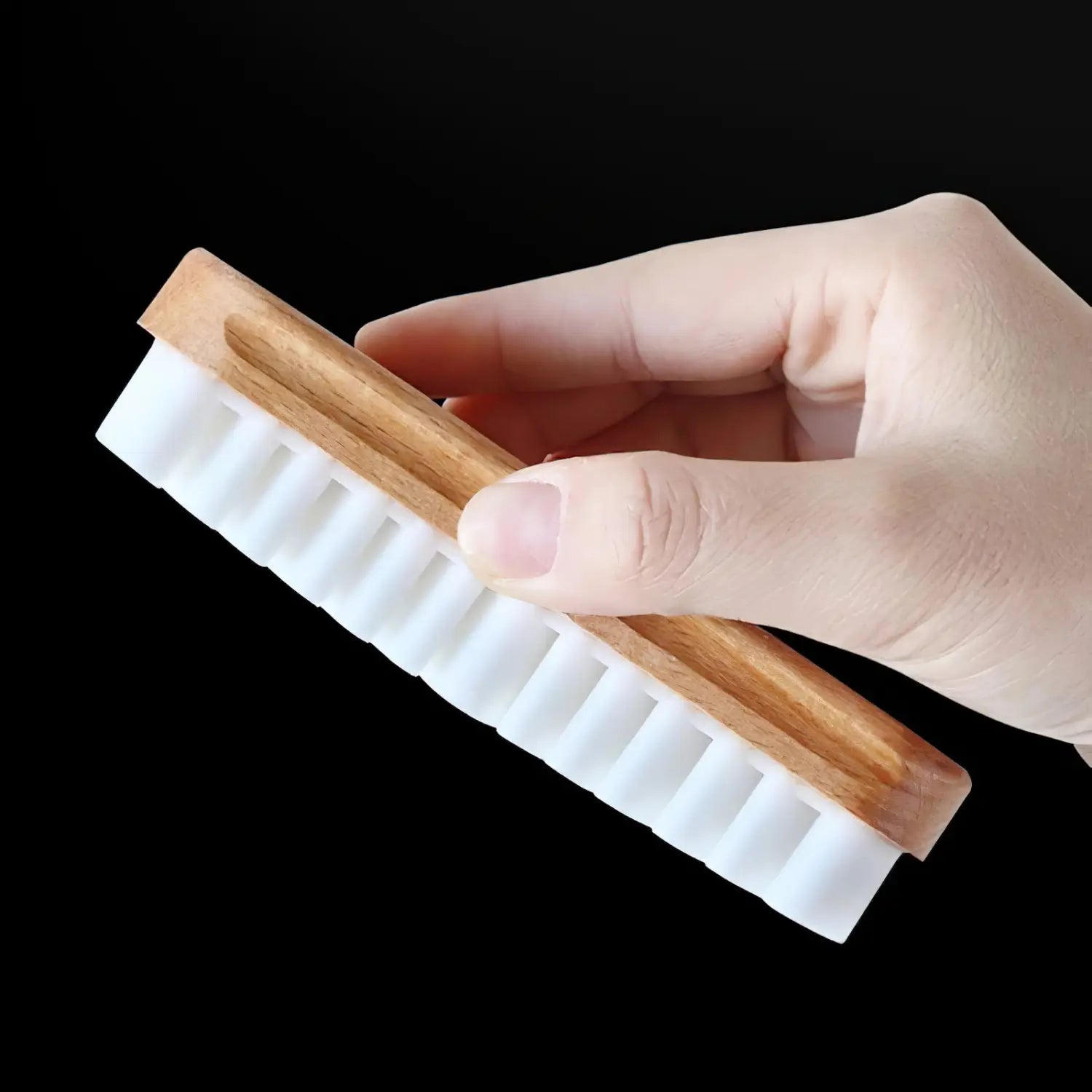 Una mano que sostiene un cepillo de limpieza para interior de coche de ante Alcántara con mango de madera y cerdas blancas densamente agrupadas.