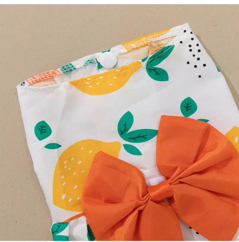 Floral dog princess dress with bow featuring a white fabric bag with yellow lemon and green leaf prints accented by a large orange bow.