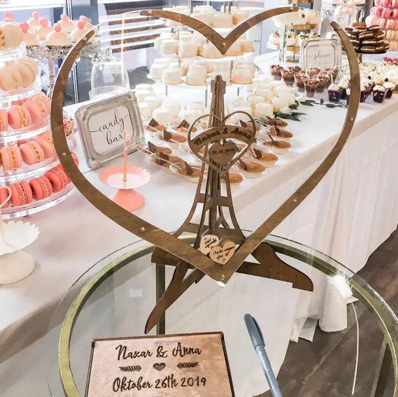 Boîte de dépôt pour livre d’or de mariage en bois rustique en forme de cœur, avec un motif miniature de la tour Eiffel et des noms et dates gravés.