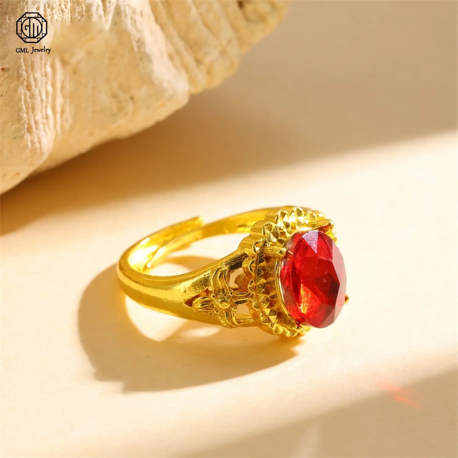 A sand gold adjustable ring featuring a matte wide band with an ornate floral pattern and a fade resistant finish, set with a prominent oval cut red gemstone.