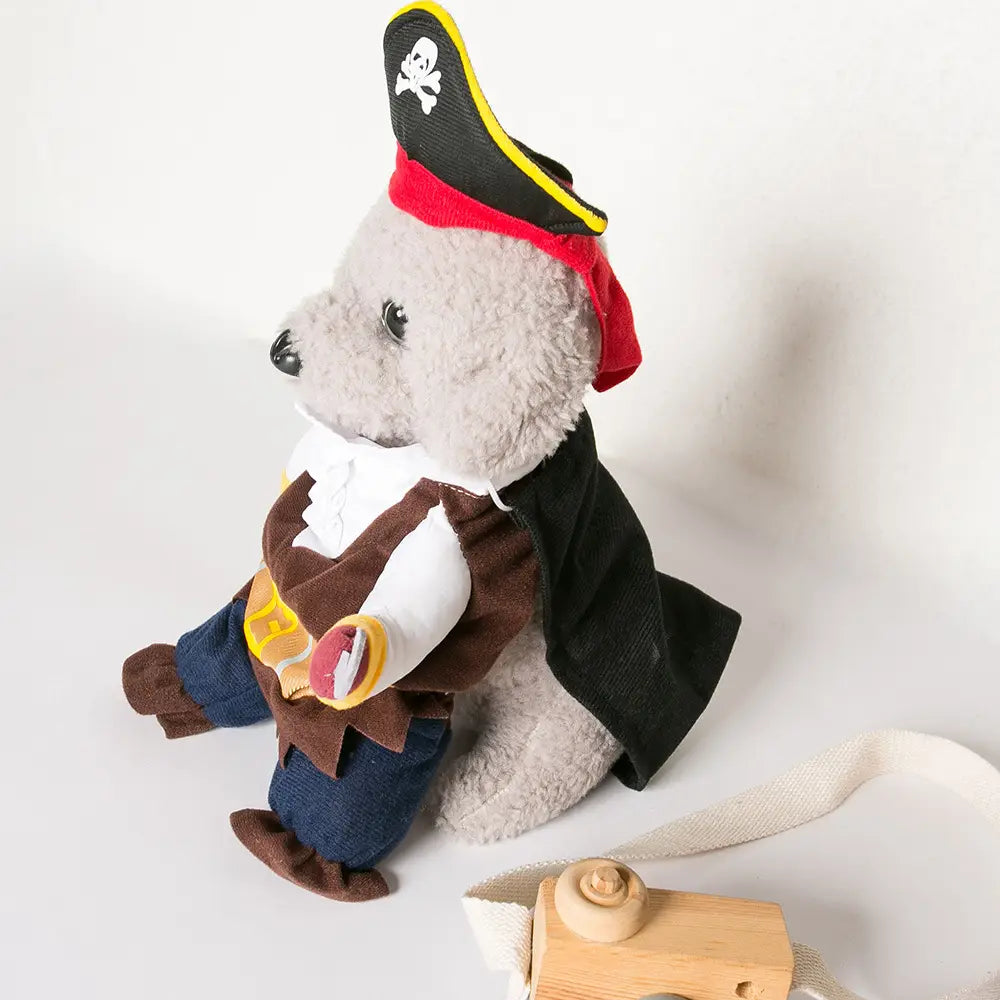 Grauer Plüsch-Teddybär, gekleidet in ein Piratenhundekostüm mit schwarzem Hut mit weißem Totenkopf und gekreuzten Knochen, brauner Weste, blauen Hosen und rotem Halstuch.