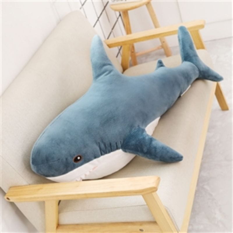 A plush blue shark stuffed animal pillow with a white underbelly and black eye designed for comfort.