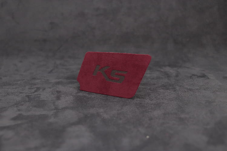 Kia K5 スエードカーボン インテリア ドアハンドルカバー用アクセサリーとして用いられる、エンボス加工のksロゴ付き赤い長方形ラバー消しゴム。