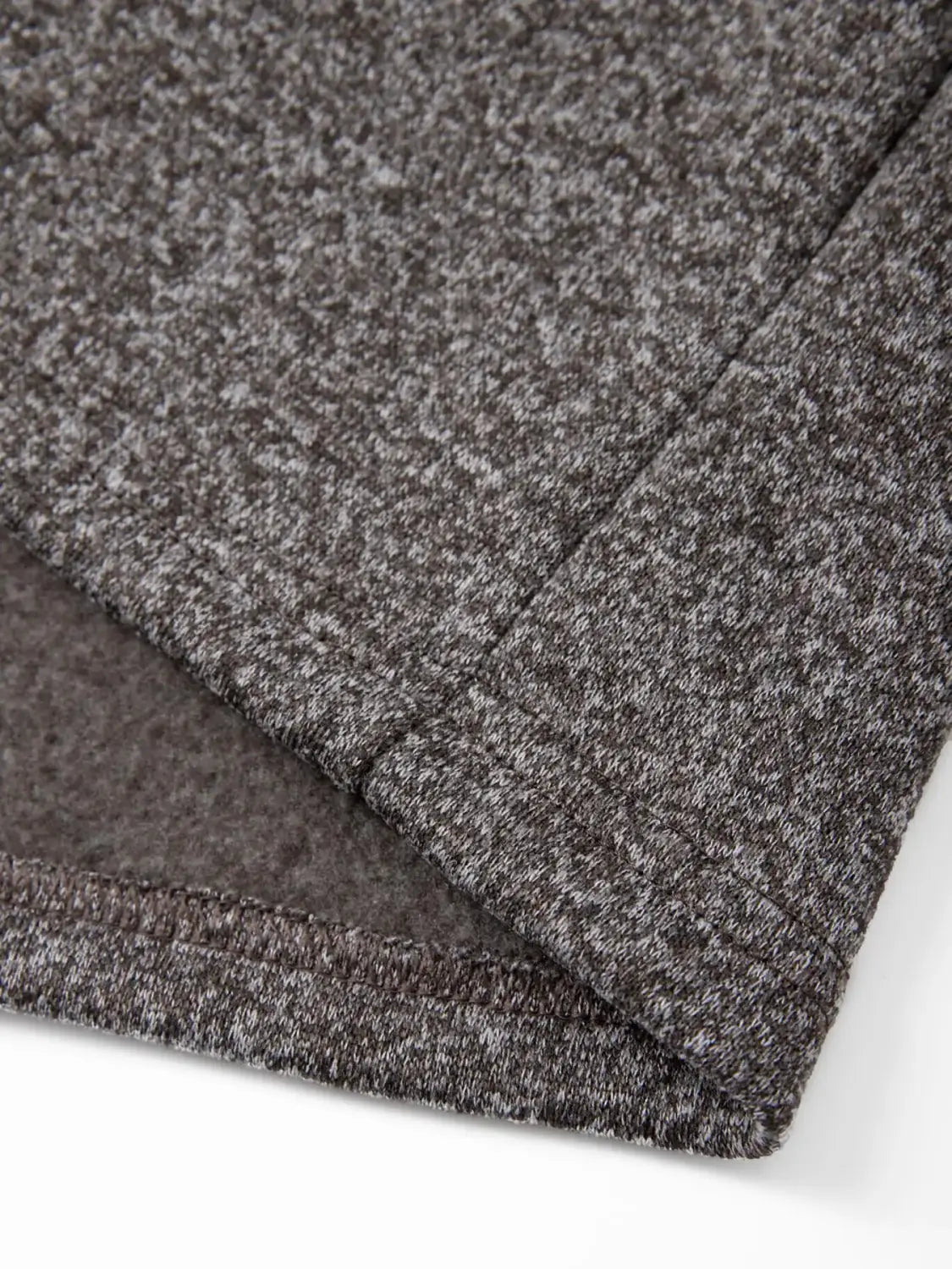 A close-up of dark gray heathered knit fabric with visible stitching along the seam on a men’s fleece lined knit hooded jacket.