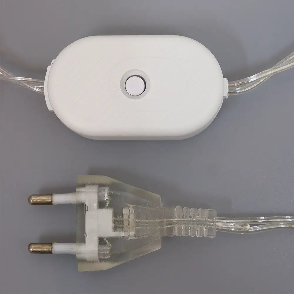 Weißer ovaler Leistungsschalter mit zentralem Druckknopf, verbunden mit transparenter Verkabelung und klarem Kunststoffstecker mit metallischen Kontakten für das LED-Rentier-Weihnachtsornamentlicht.