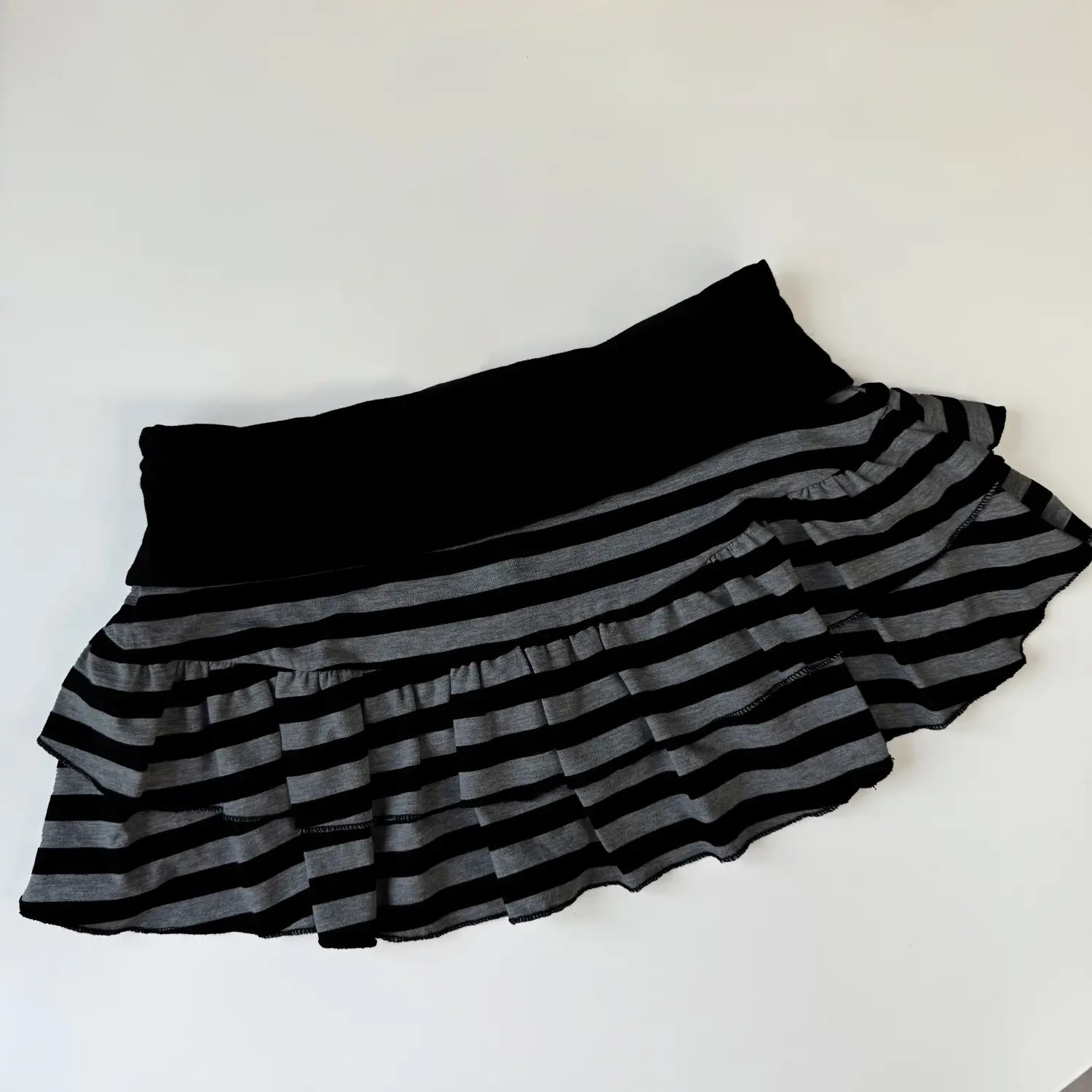 Jupe courte à volants rayée noir et gris, avec une ceinture élastique unie noire, conçue pour un port confortable et une allure élégante