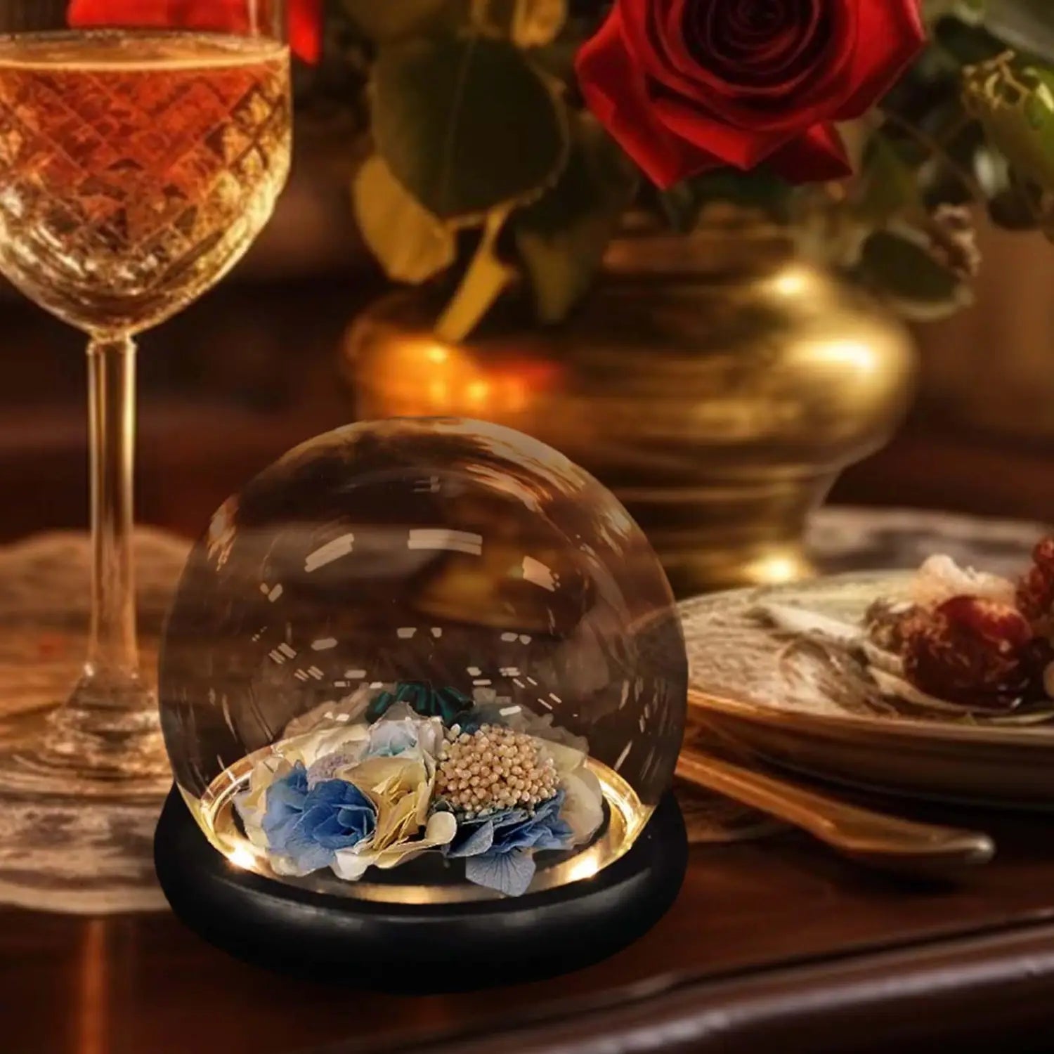 A clear glass display dome with a black base housing a dried floral arrangement in blue and gold colors.