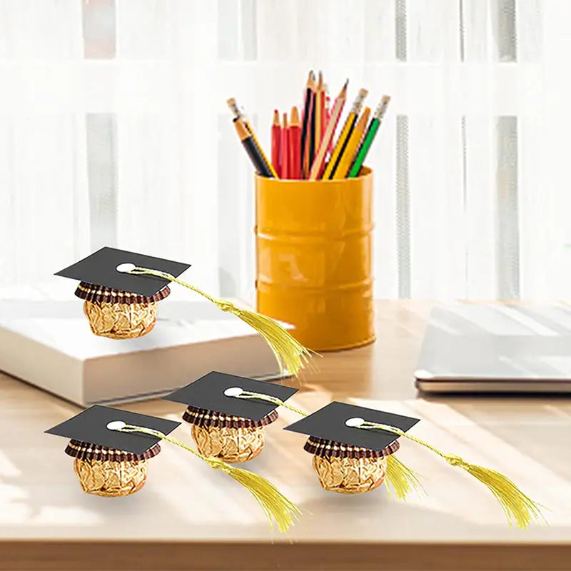 Caramelos de chocolate envueltos en dorado, decorados con mini birretes de graduación negros y borlas amarillas para decoraciones de chocolate y caramelos de birrete de graduación 2025.