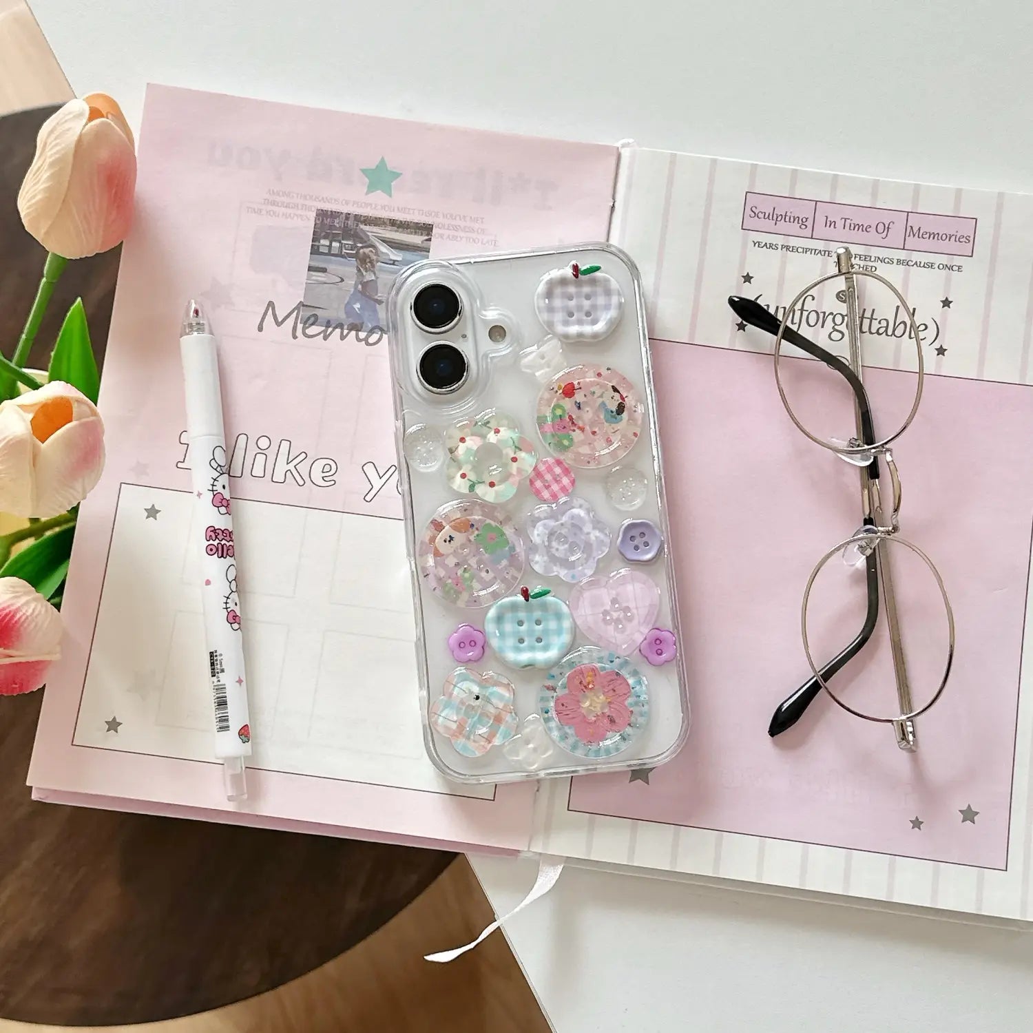 Funda transparente para iPhone con adornos de botones coloridos en tonos pastel, con diseños en forma de manzana y motivos florales en la parte posterior.