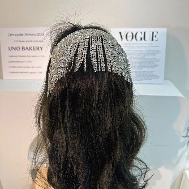 Bandeau en perles et strass perlé argenté, au motif scintillant qui se drape avec élégance sur des cheveux foncés ondulés, pour un usage de mariée.