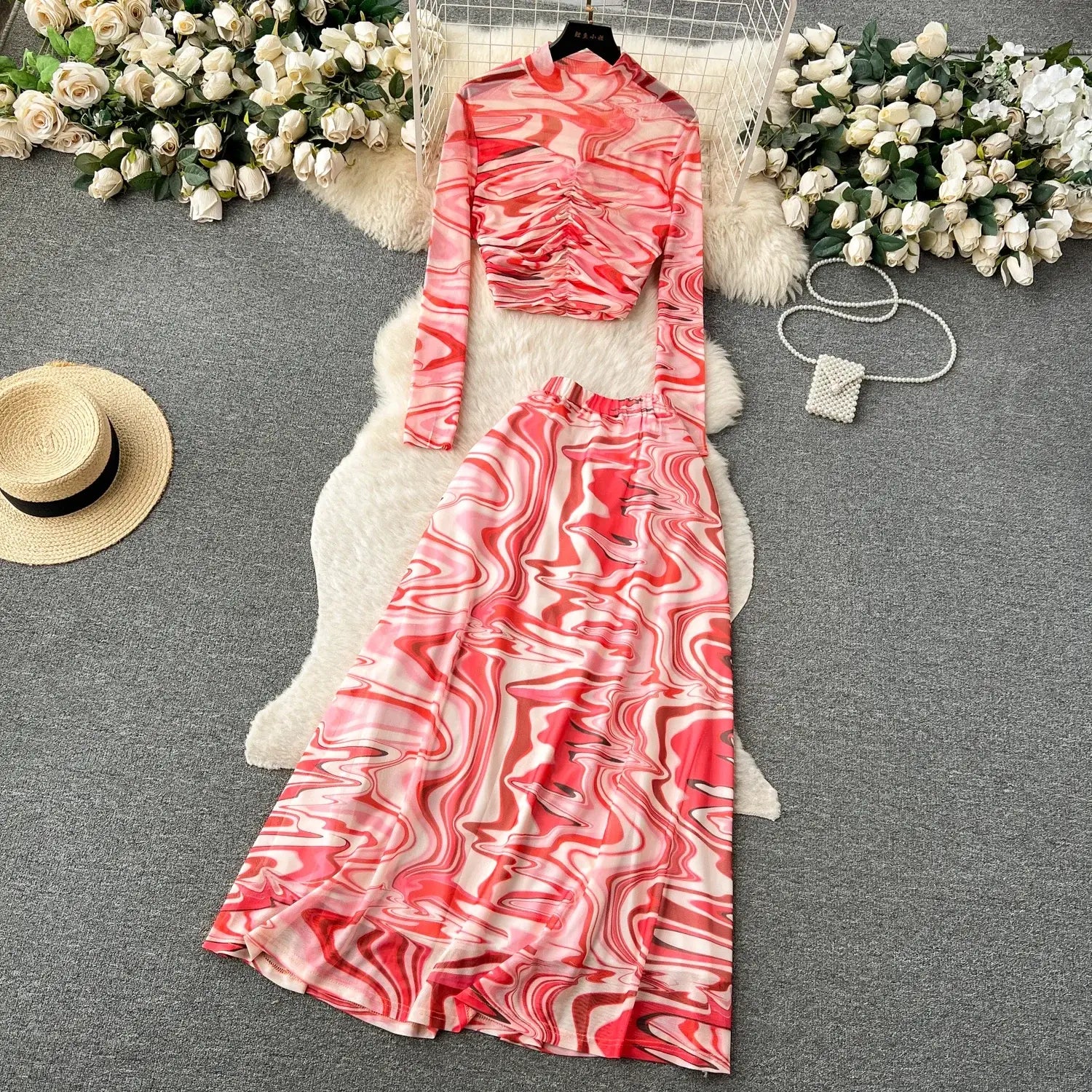 a flowing two-piece mesh skirt set in vibrant pink and white marble print featuring a fitted long-sleeved top with ruching at the bust and a matching high-waisted skirt with elastic closure type