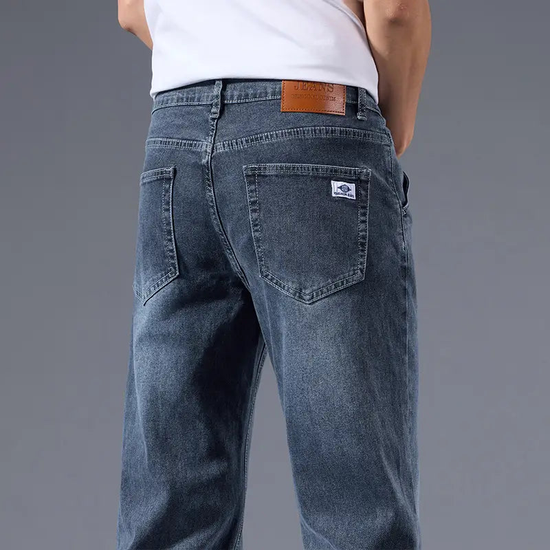 Jeans rétro délavés coupe droite ample pour hommes en denim bleu foncé, montrés depuis l’arrière, avec un empiècement de marque en cuir brun sur la ceinture et une petite étiquette blanche sur la poche arrière.