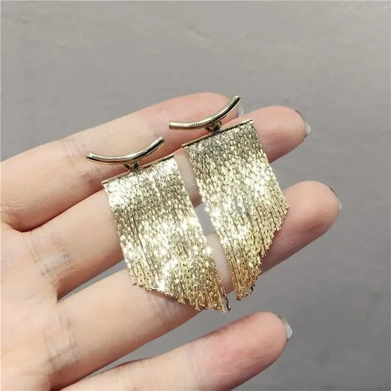 Boucles d’oreilles déclaration à frange en or, avec une frange scintillante couleur or, une finition métallique texturée et des crochets supérieurs incurvés.