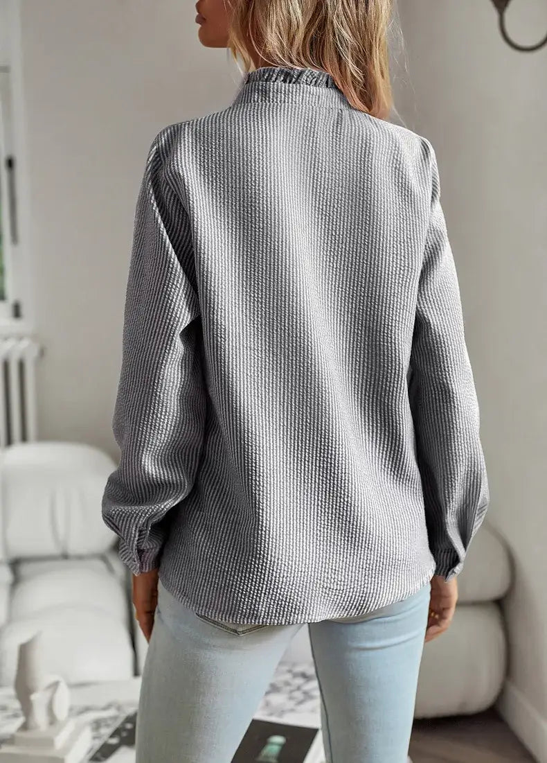 Blusa de algodón acanalado gris con cuello clásico y mangas largas, mostrada junto a una blusa blanca de textura con manga larga y volantes.