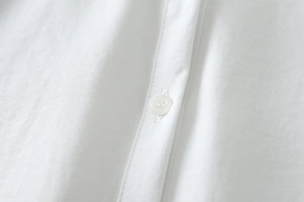 Ein kleiner, durchscheinend-weißer Knopf mit dezentem Schimmer auf der Knopfleiste einer Damen-Casualbluse aus Baumwollmischgewebe mit langen Ärmeln in knackigem Weiß.