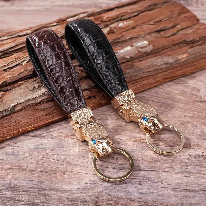 Two crocodile-patterned leather keychains with gold-toned snake head charms featuring blue gemstone eyes for luxury car key rings.