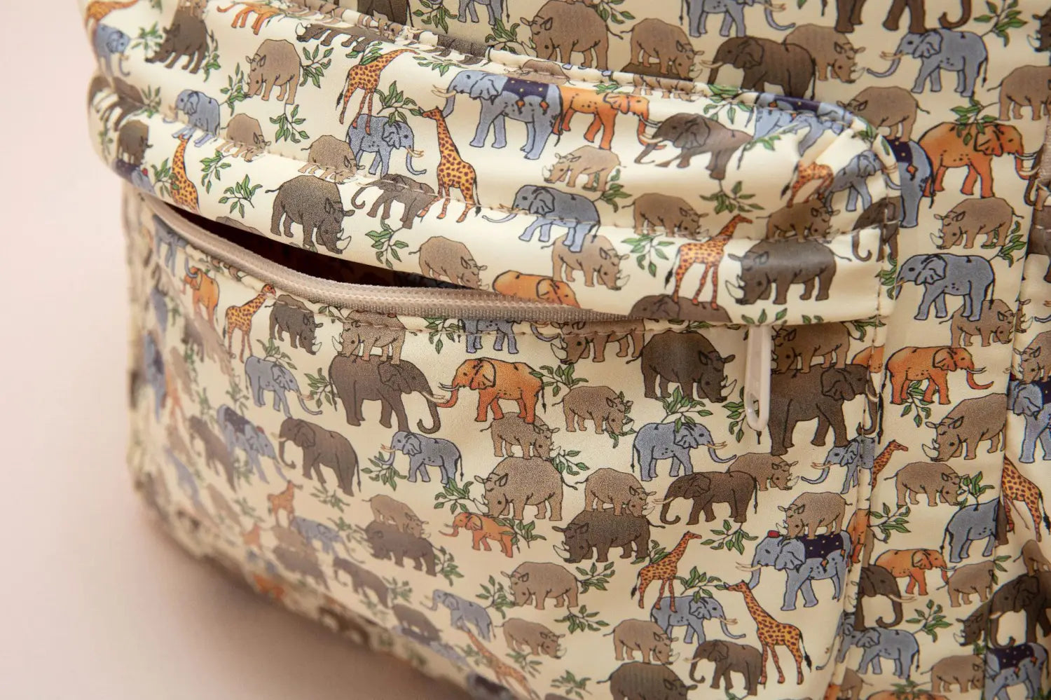 Un sac à dos crème pour enfants à thème dinosaure, avec un motif ludique d’éléphants et de girafes en brun, gris, bleu, orange et beige, conçu comme un sac d’école pastel.