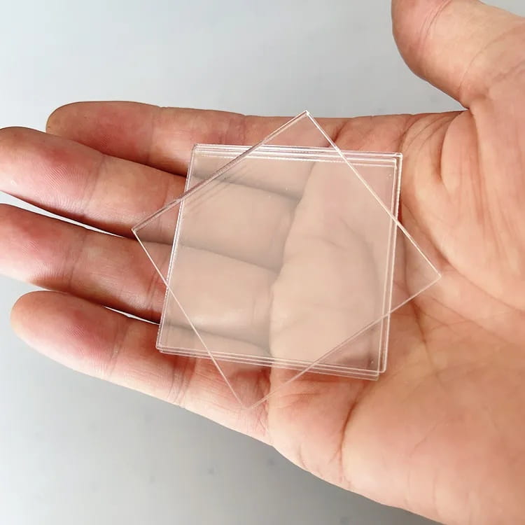 une main tenant des plaques d’acrylique carrées transparentes provenant d’un kit de bricolage DIY de magnets de réfrigérateur personnalisés pour créer des magnets de réfrigérateur personnalisés.