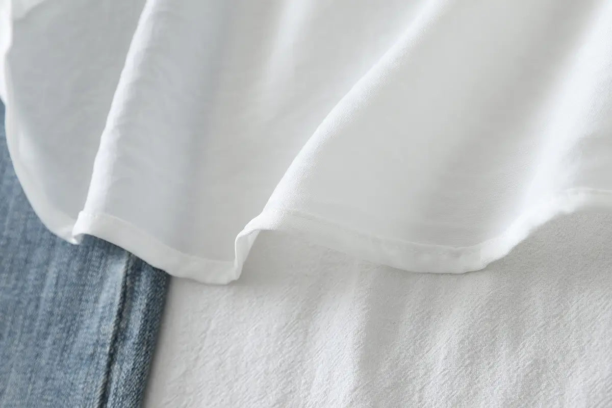 weißes Baumwollmischgewebe für die Damen-Casualbluse mit langen Ärmeln mit weichen, fließenden Falten neben einem Jeansartikel, der die Materialstruktur und den Farbkontrast veranschaulicht