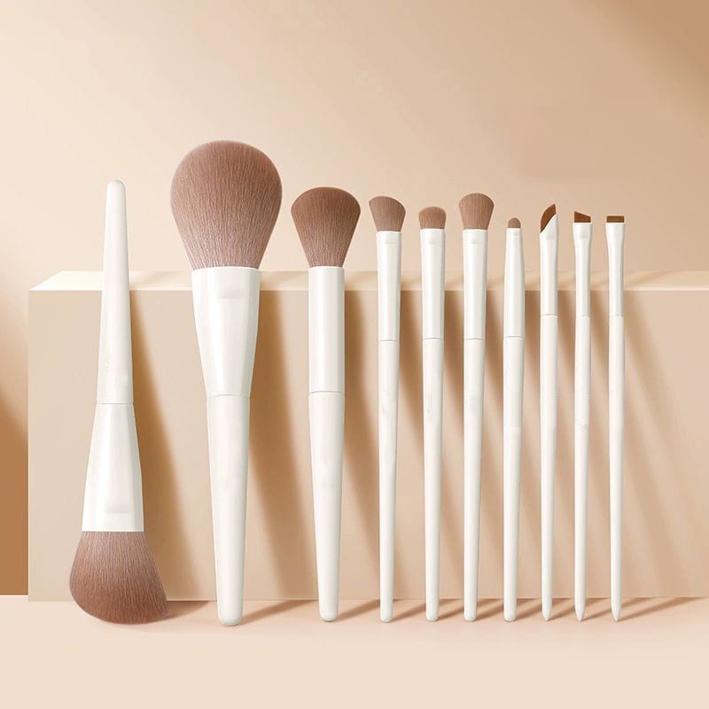 Lot de dix pinceaux de maquillage à manches blancs, aux poils bruns coniques doux, disposés avec soin sur une surface beige, issus d’un ensemble d’accessoires cosmétiques blanc et or de 12 pièces.