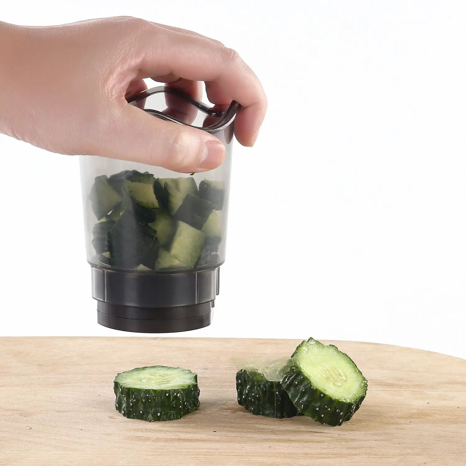 Transparent plastic handheld fruit and vegetable chopper slicer with black base and handle filled with chopped green cucumbers