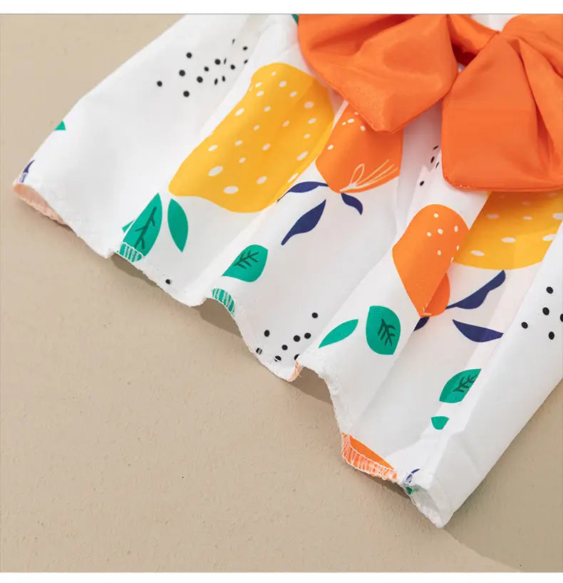 White skirt floral dog princess dress with playful citrus fruit and leaf pattern in yellow orange green and navy blue accented by an oversized orange bow at the waist.