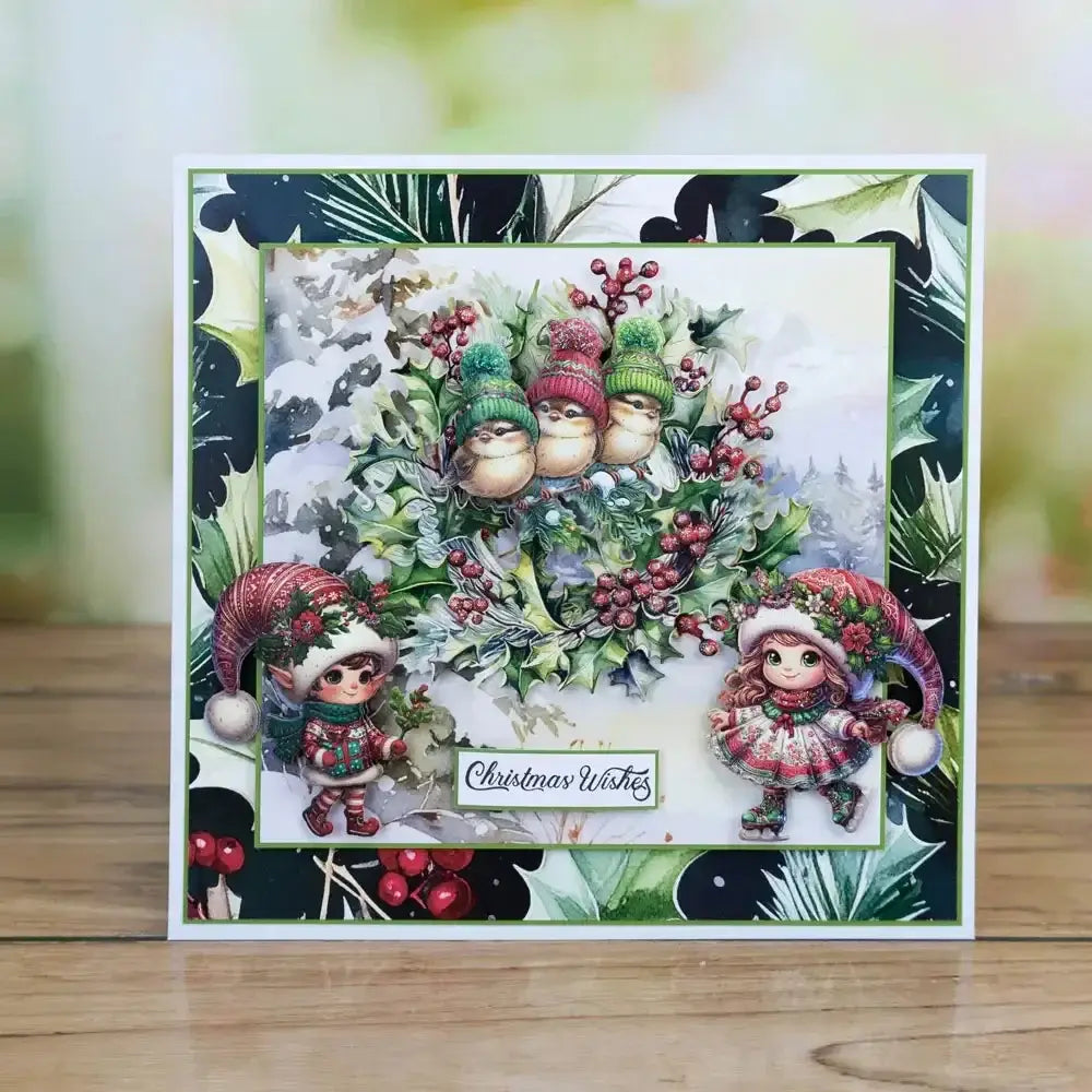 a festive christmas metal cutting die and stamp set featuring illustrated elves and birds nestled in a holly wreath with red berries and green foliage on a layered design