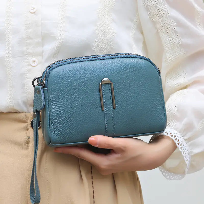 Tealfarbene Umhängetasche-Wallet aus echtem Leder für Damen mit silberfarbenem Metallschnallenverschluss und passendem Handgurt.