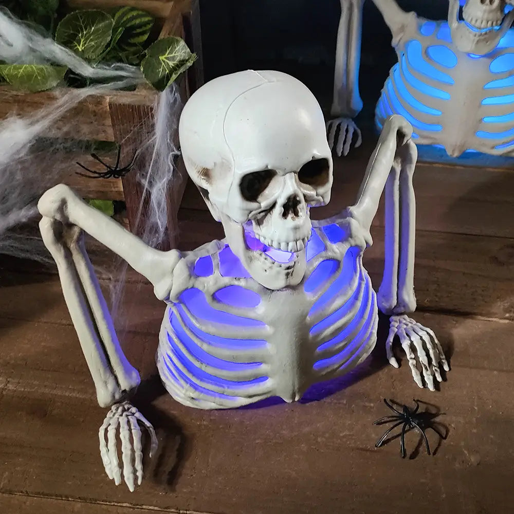 Un accesorio de Halloween de esqueleto luminoso hecho de plástico blanco, con iluminación interna azul y brazos y manos articulados, apoyados sobre una superficie de madera.