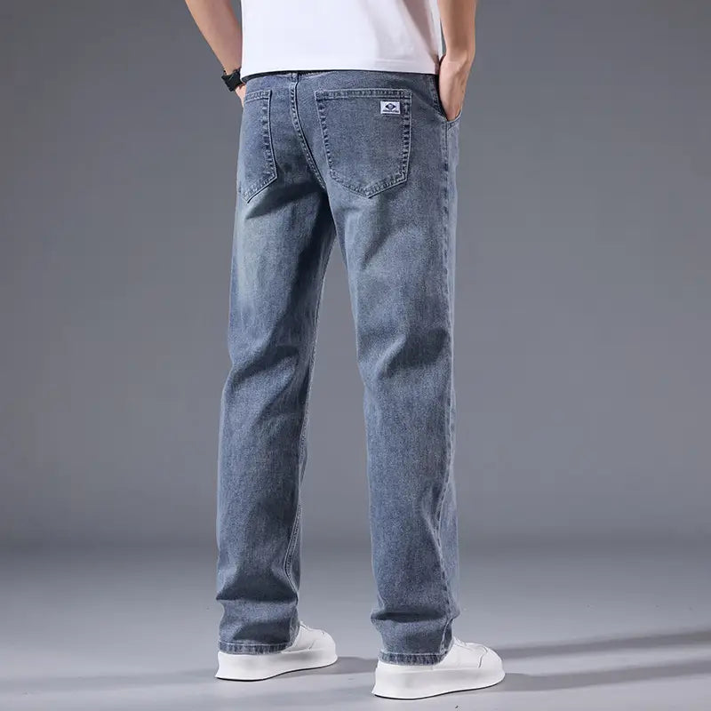 Jeans rétro délavés coupe droite ample pour hommes en denim clair, avec une coupe droite, une décoloration subtile, des poches arrière classiques et un petit empiècement de marque sur la poche droite, montré depuis l’arrière.