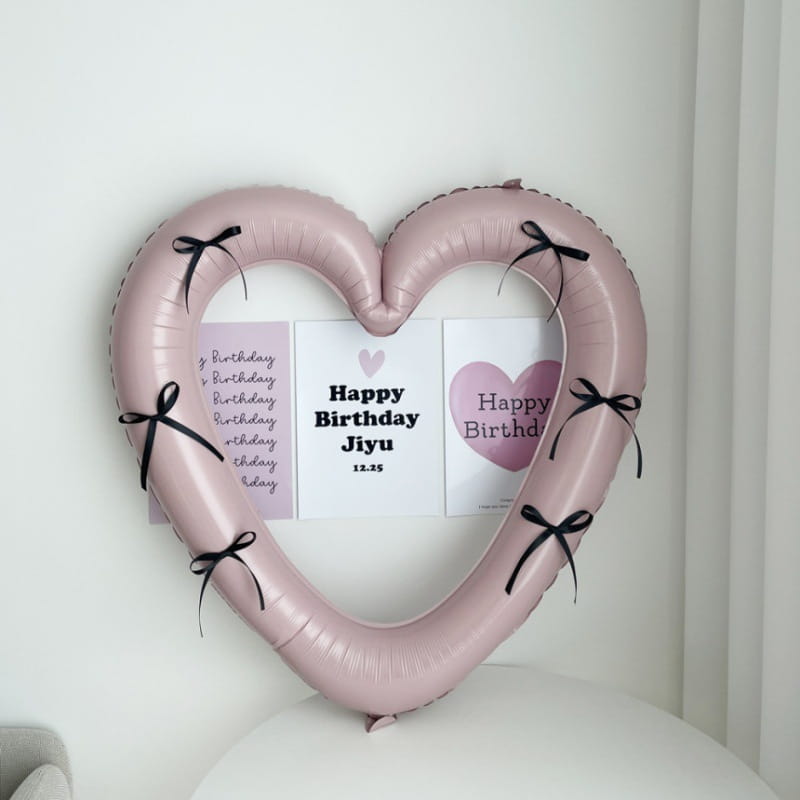 Un globo de lámina con forma de corazón rosa suave para marco de foto de 40 pulgadas, adornado con cintas negras y sujetando tarjetas de cumpleaños