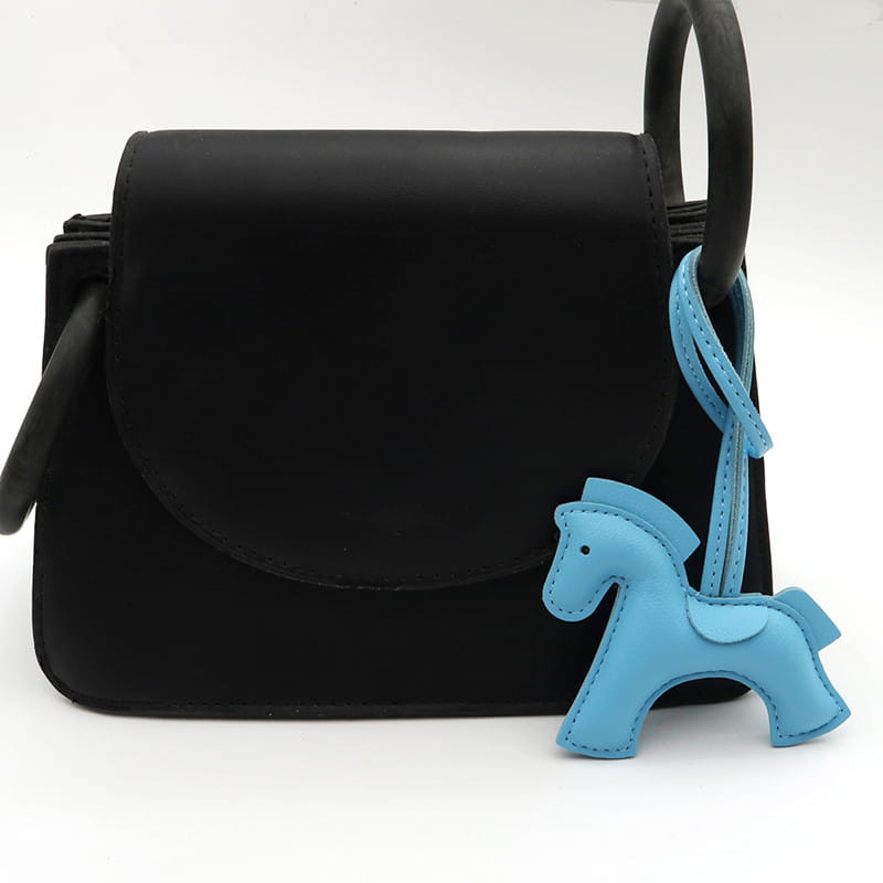 Sac en cuir noir porté en bandoulière avec un porte-clés en cuir bleu clair en forme de cheval fixé à la poignée.