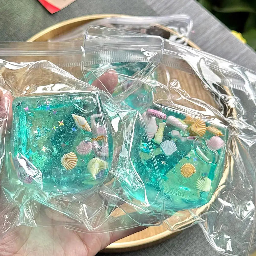 Un cube sensoriel à effet anti-stress pour l’océan, cadeau attentionné, fabriqué en résine de couleur turquoise, avec des coquillages intégrés, des étoiles de mer et du glitter, créant un objet souvenir sur le thème de la mer.
