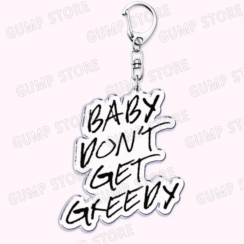 Silver acrylic Tate Mcrae keychain with baby dont get greedy in bold black graffiti-style lettering, a music fan gift accessory.