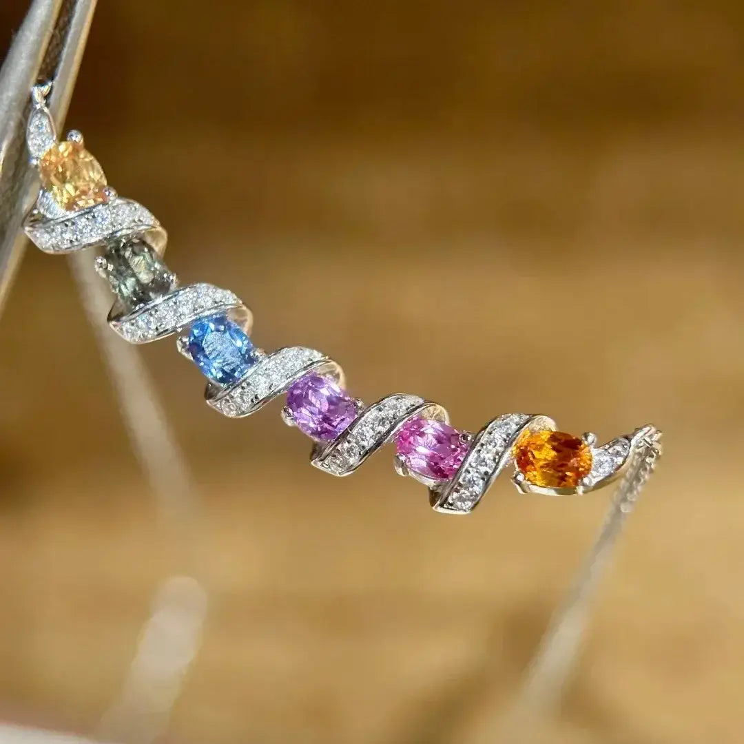 Un délicat collier en argent présentant un design de bracelet en spirale avec cinq pierres précieuses vibrantes en saphir jaune, spinelle verte, saphir bleu, saphir violet et saphir rose, entourées de diamants étincelants.