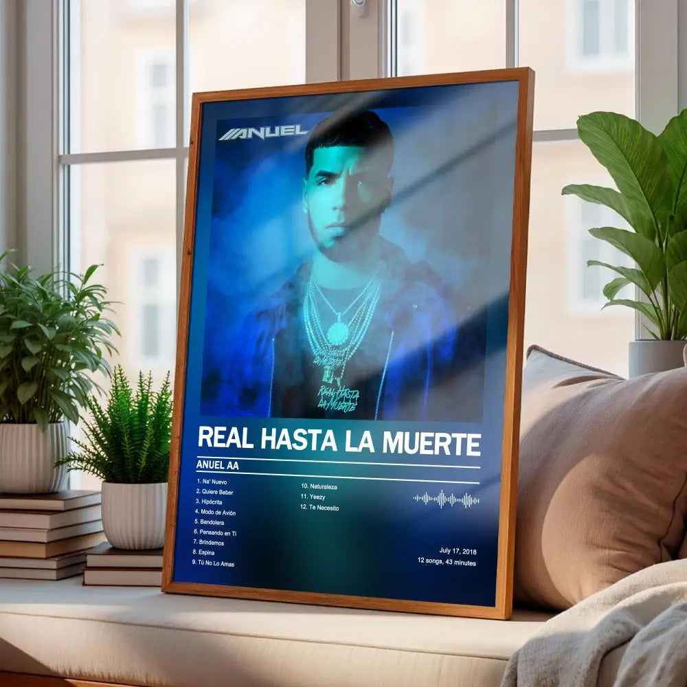 a framed wall art print featuring a blue-toned portrait of artist anuel aa with his album title real hasta la muerte in white text on a dark background, displayed in a light brown wooden frame, ideal for modern style art home decor.