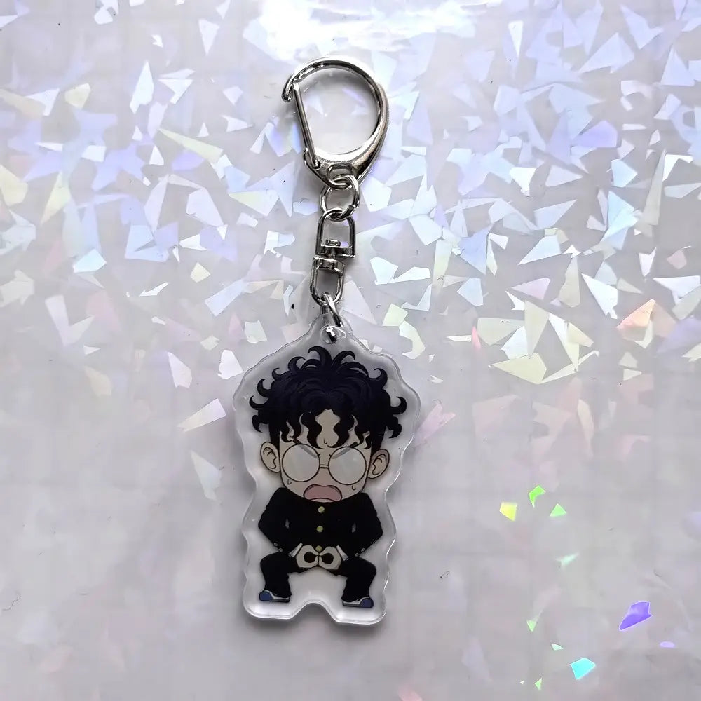 黒い縮れ毛、丸いメガネ、黒い衣装を身に着けた、カートゥーンキャラクター ももをあしらったクリアアクリル『ダンダダン』アニメキーホルダー。