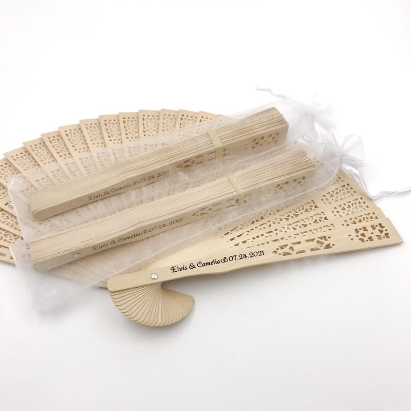 Éventail pliant en bois beige avec des motifs de découpes fines, de style dentelle, et des noms et une date gravés personnalisés comme faveurs de mariage.